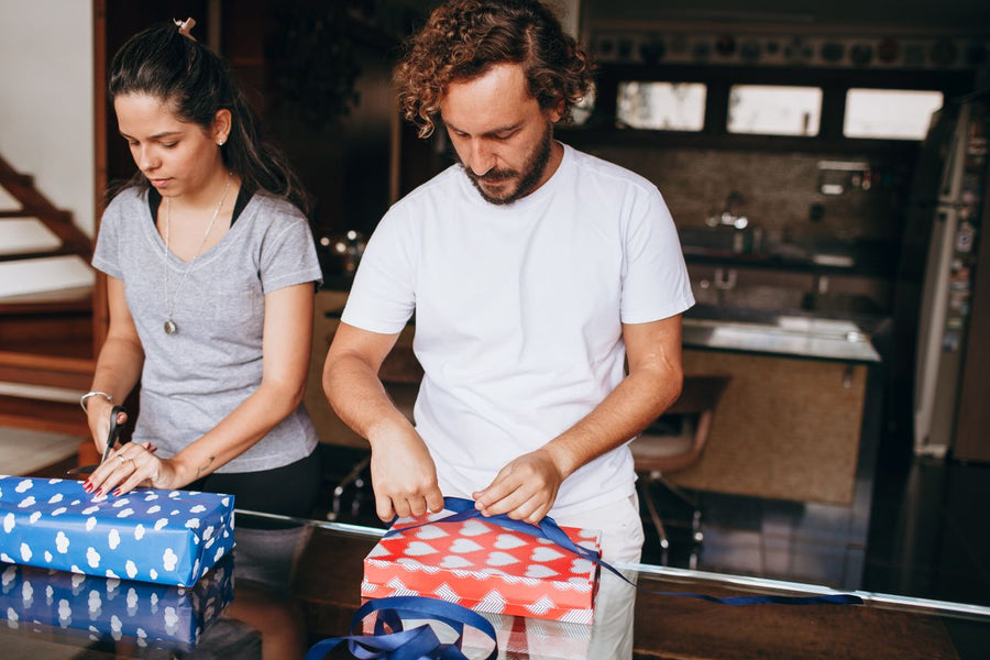 A couple wrapping gifts together at a home table.